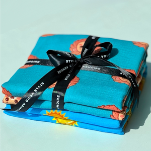Two folded organic muslin swaddles with high contrast sun and lion prints.
